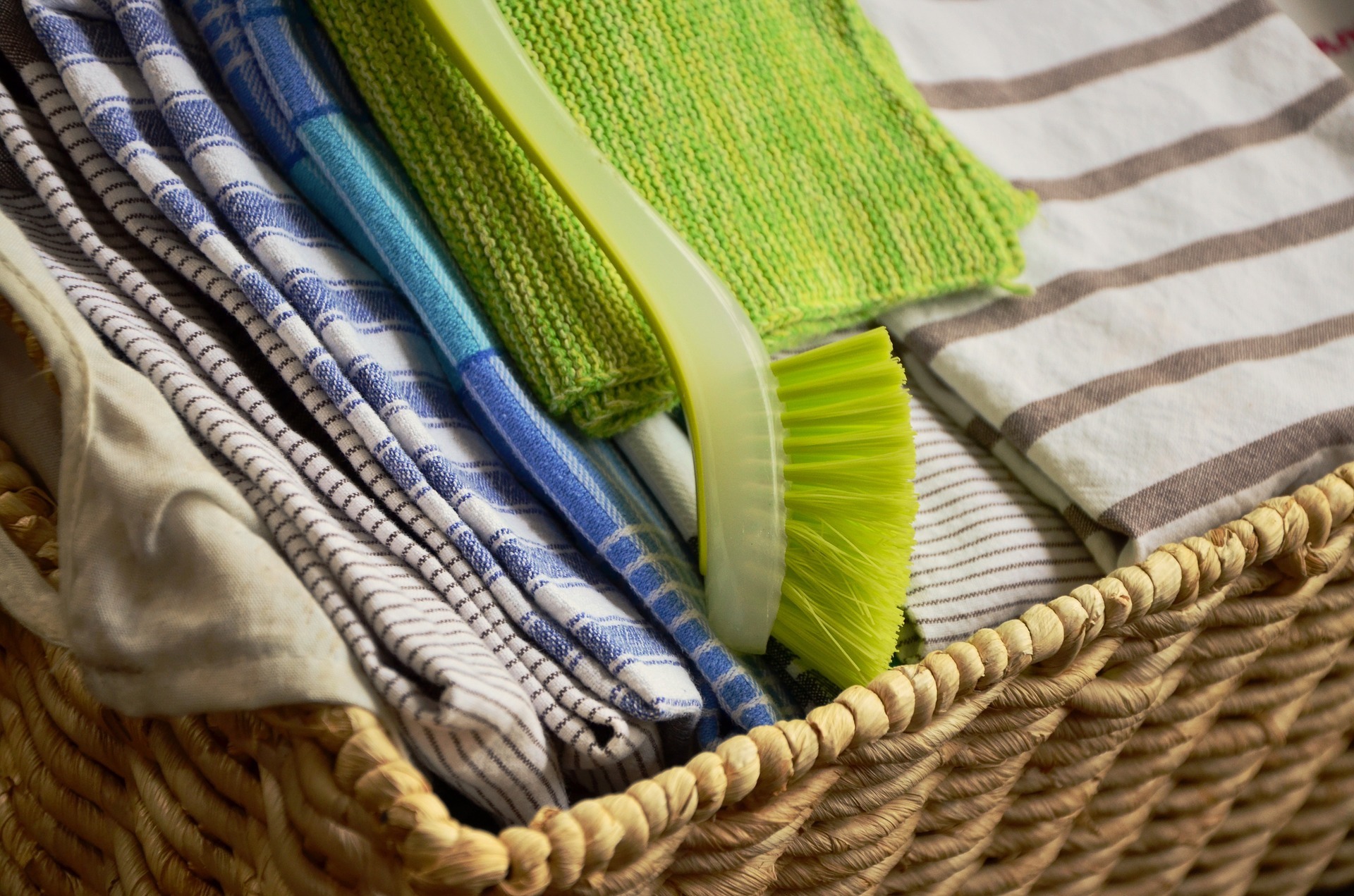 inside the basket are sets of kitchen towel and a green brush