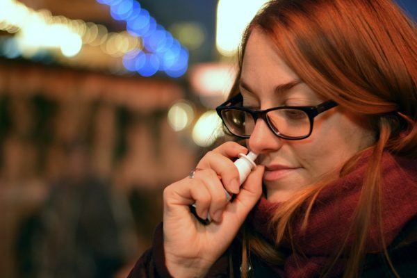 A woman using a nasal spray instead of a facial massage for sinuses
