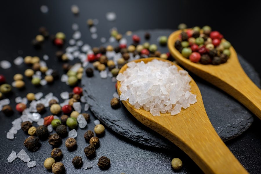 Two wooden spoons, one that is filled with pickling salt and one with other spices