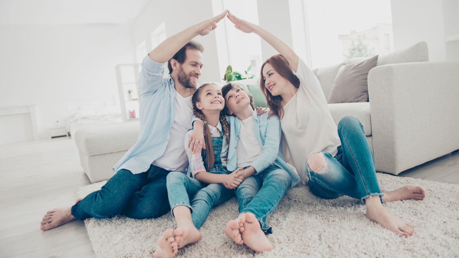 Stylish full family with two kids sitting on carpet, mom and dad making roof figure with hands arms over heads