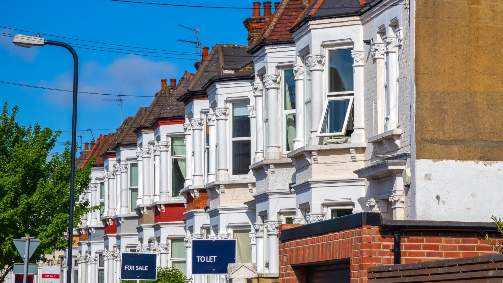 A row of typical British terraced houses around Kensal Rise in London with estate agent boards