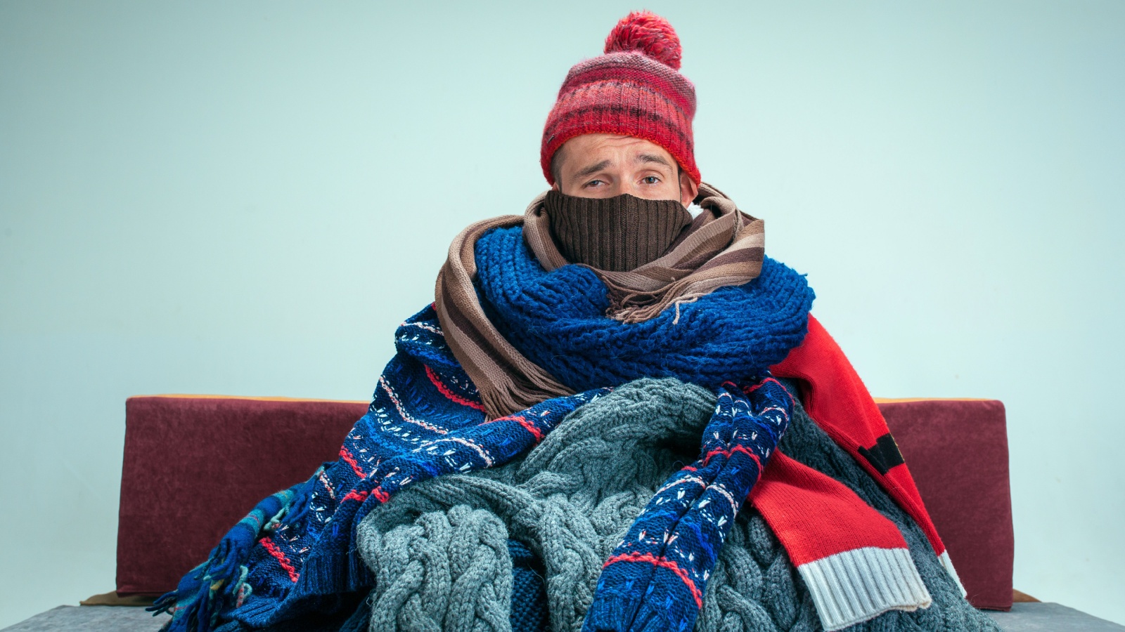 sick man with flue sitting on sofa at home or studio covered with knitted warm clothes. Illness, influenza, pain concept. Relaxation at Home. Healthcare 