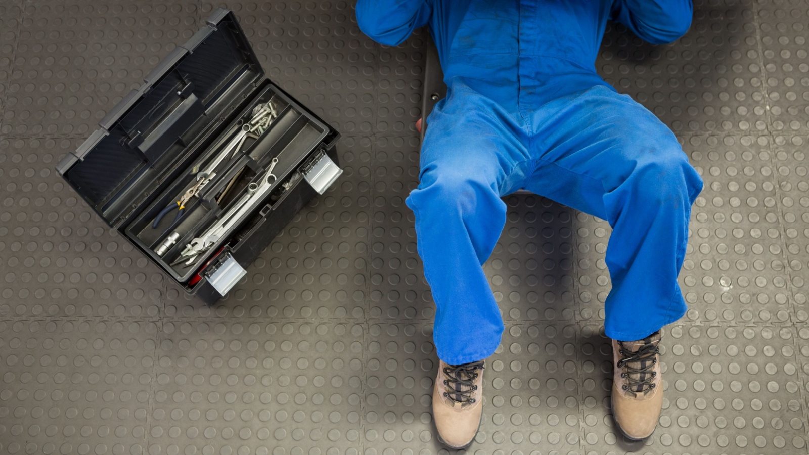 Man working under a car with a toolbox beside him