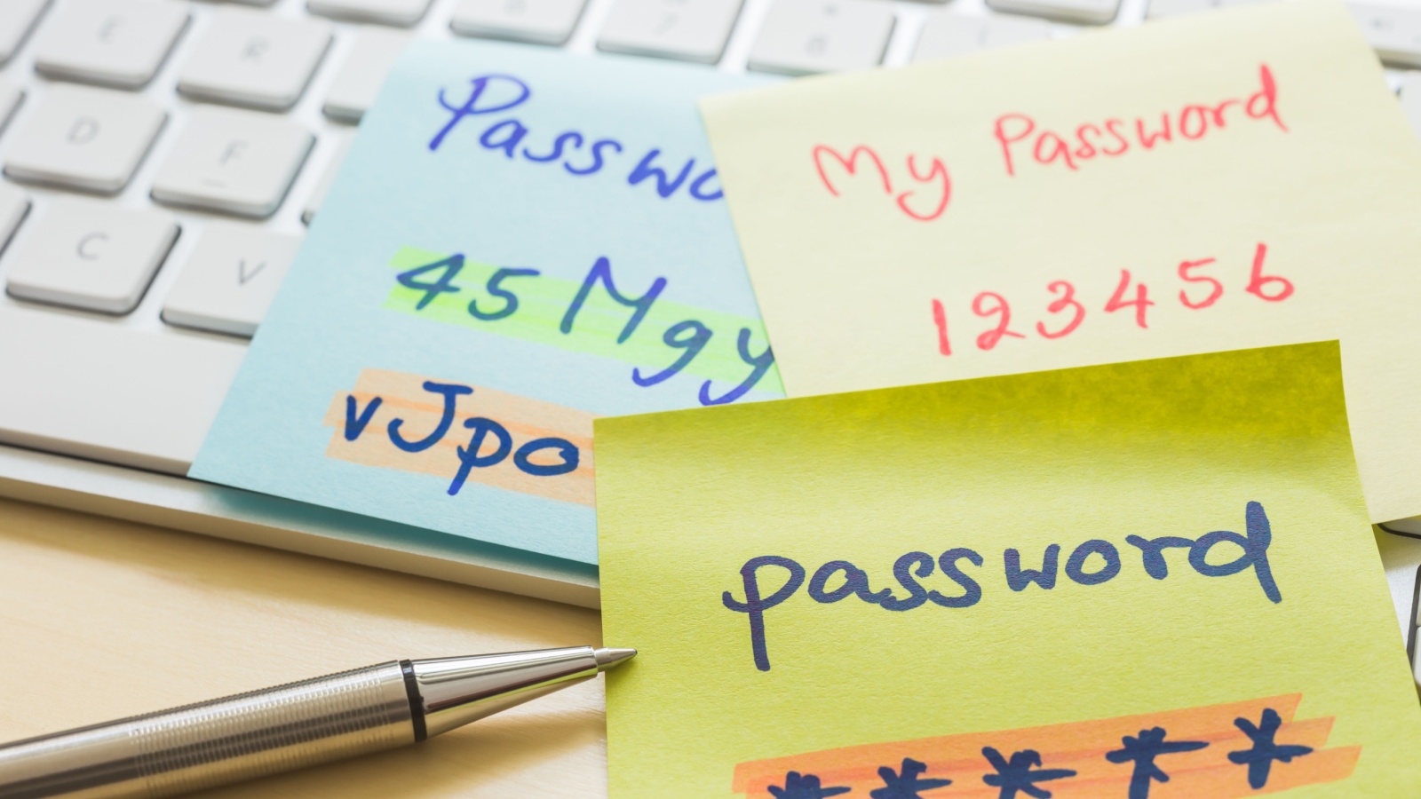 Silver pen pointing at handwriting passwords with highlight colors written on paper notes at modern white keyboard with office table on background. Data privacy management and cyber security