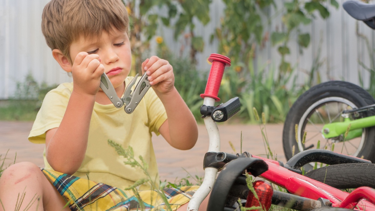 Kid opening multi tool while sitting near the bike. Boy fixing bicycle. Summer vacation background. Summer camps background. Transport and children. Cycle on the grass. Boy playing outside.