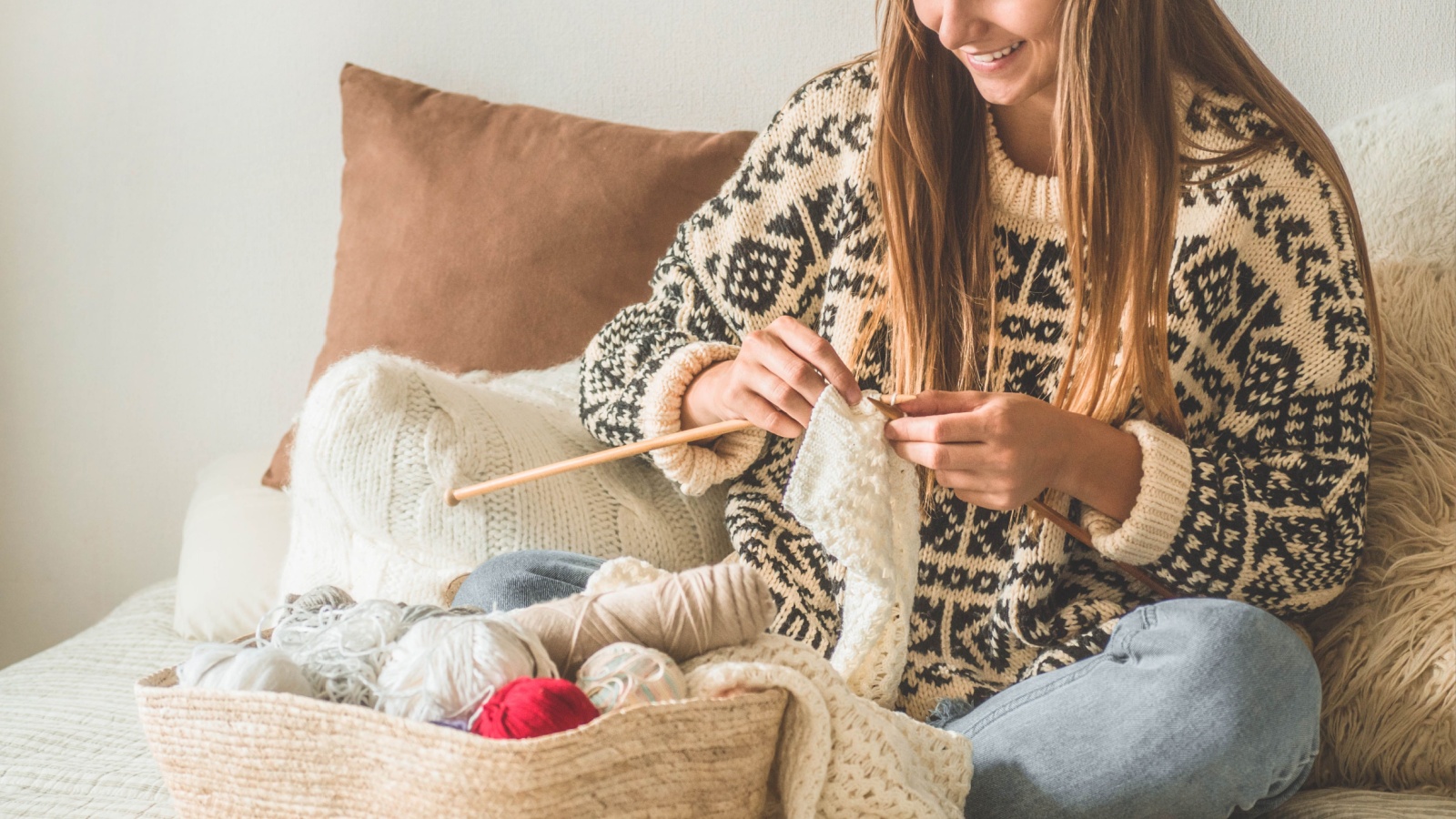 Beautiful girl knits a warm sweater on the bed. Knitting as a hobby. Accessories for knitting.