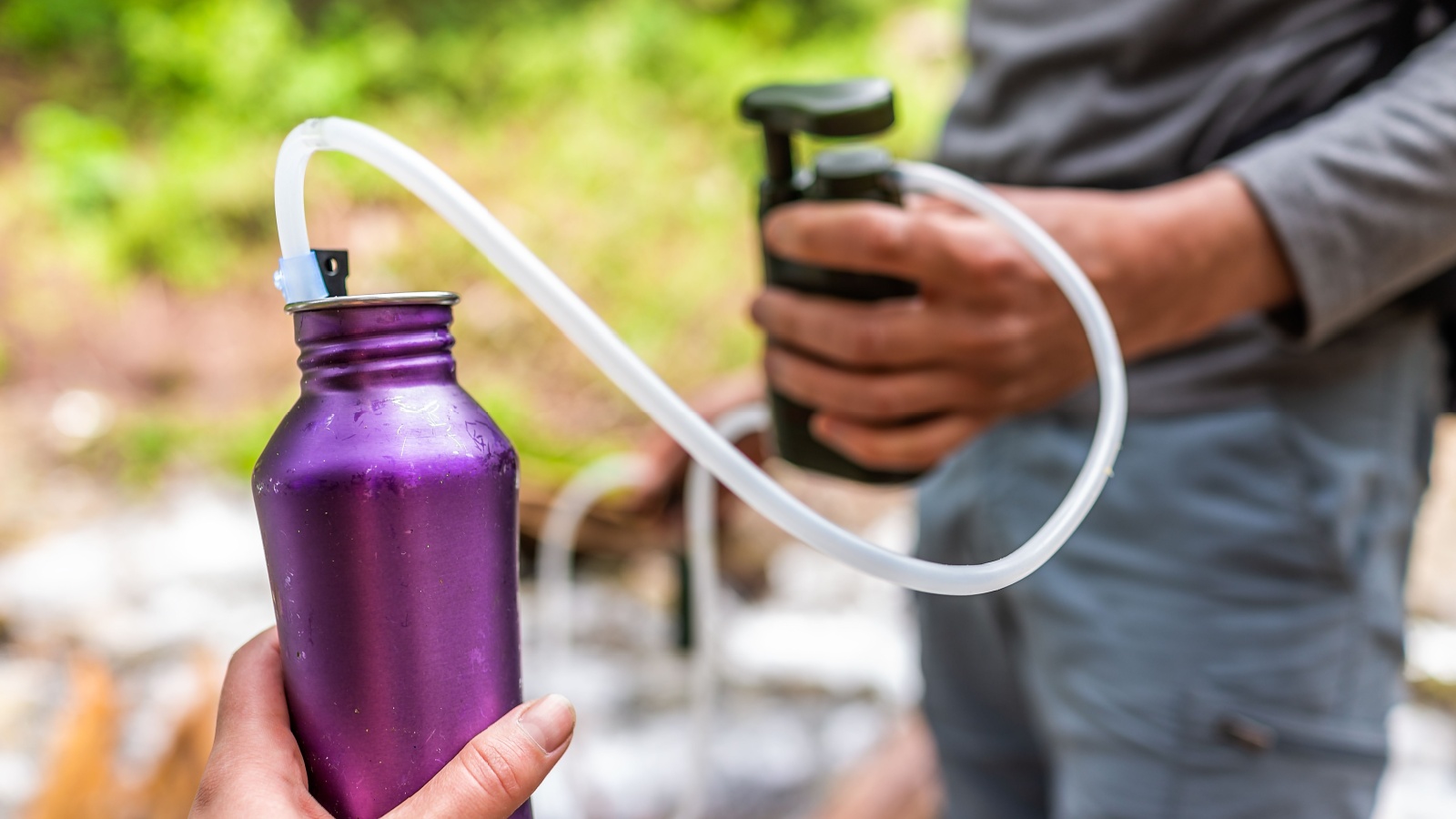 Man and woman couple using water filter on hiking trail river in Colorado to purify drinking water into bottle