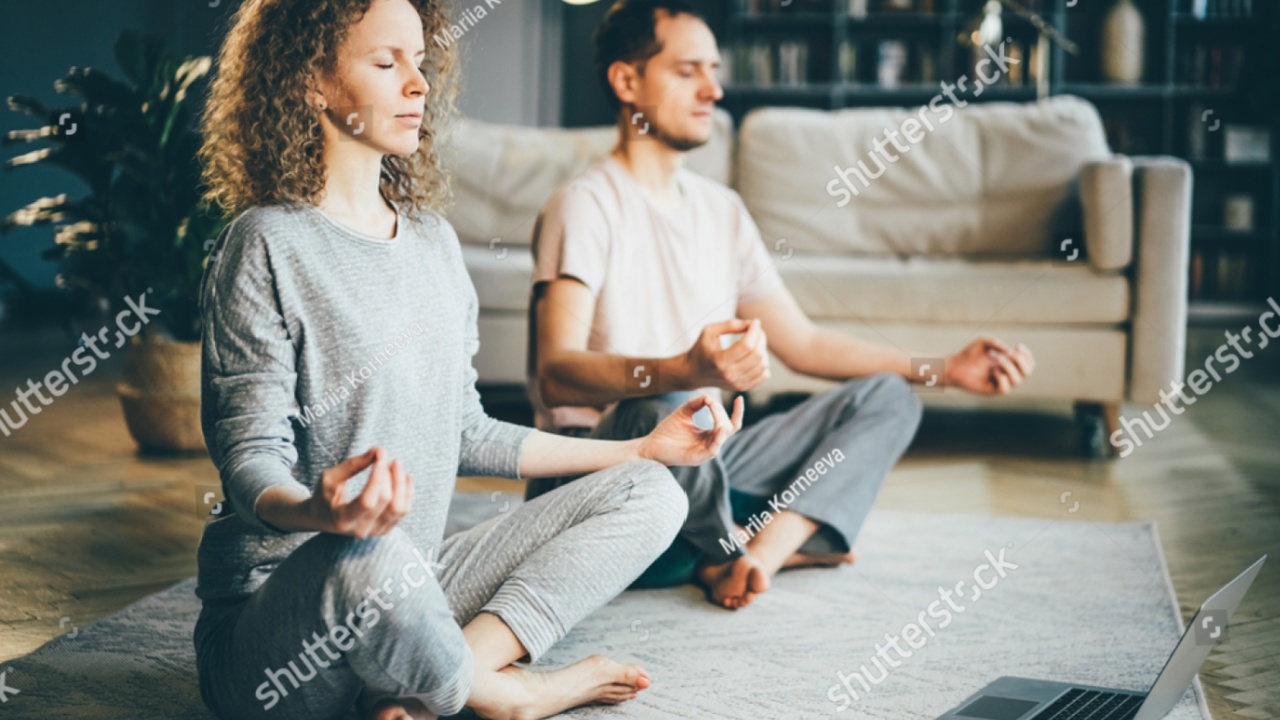 Calm couple in pajamas meditating, listening spiritual practices lessons on laptop, sitting on lotus pose at home. Yoga, mindfulness