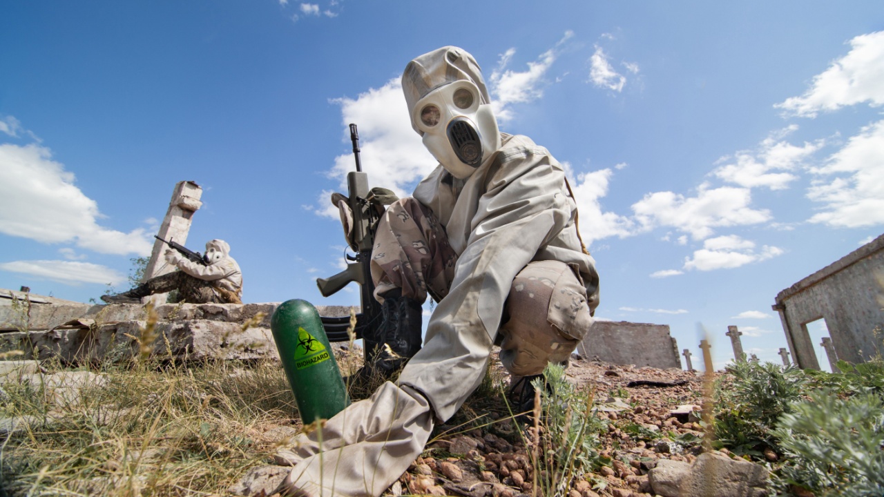 Two soldiers in the gas masks and protective clothes are testing biological weapon on the ruined background.