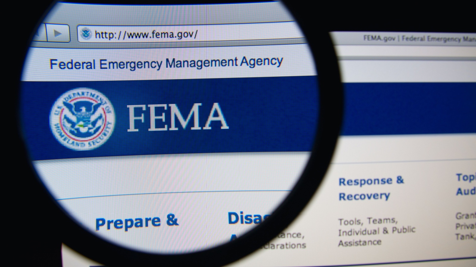 Photo of Federal Emergency Management Agency homepage on a monitor screen through a magnifying glass. FEMA is an agency of the US Department of Homeland Security.