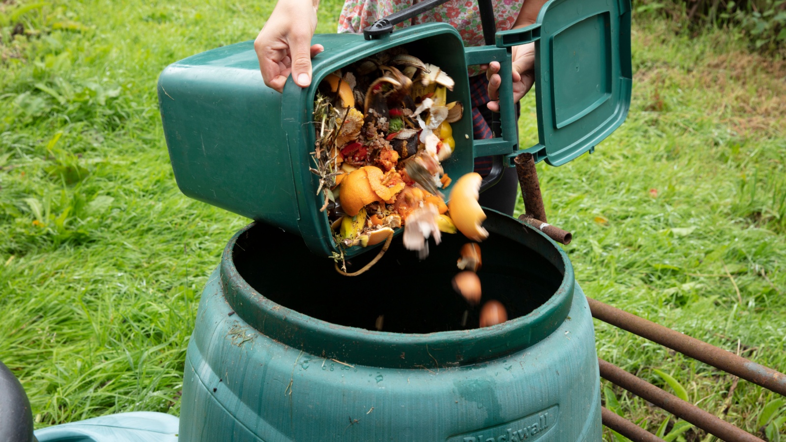 A woman emptying a home composting bin into an outdoor compost bin to reduce waste