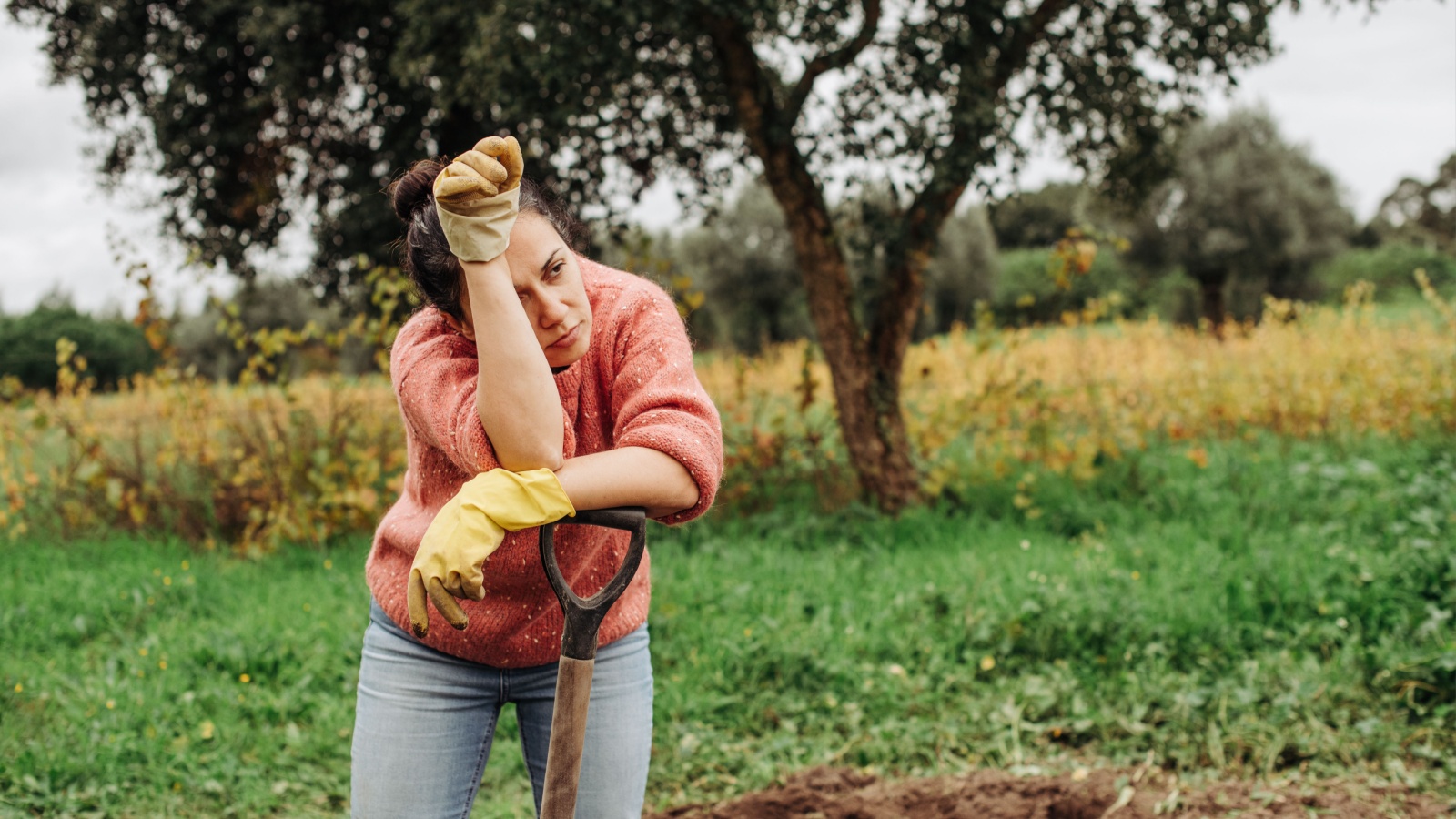 Female farmer looking tired after day of work on the field. Woman standing at vegetable garden feeling exhausted from hard work in agriculture, mental health