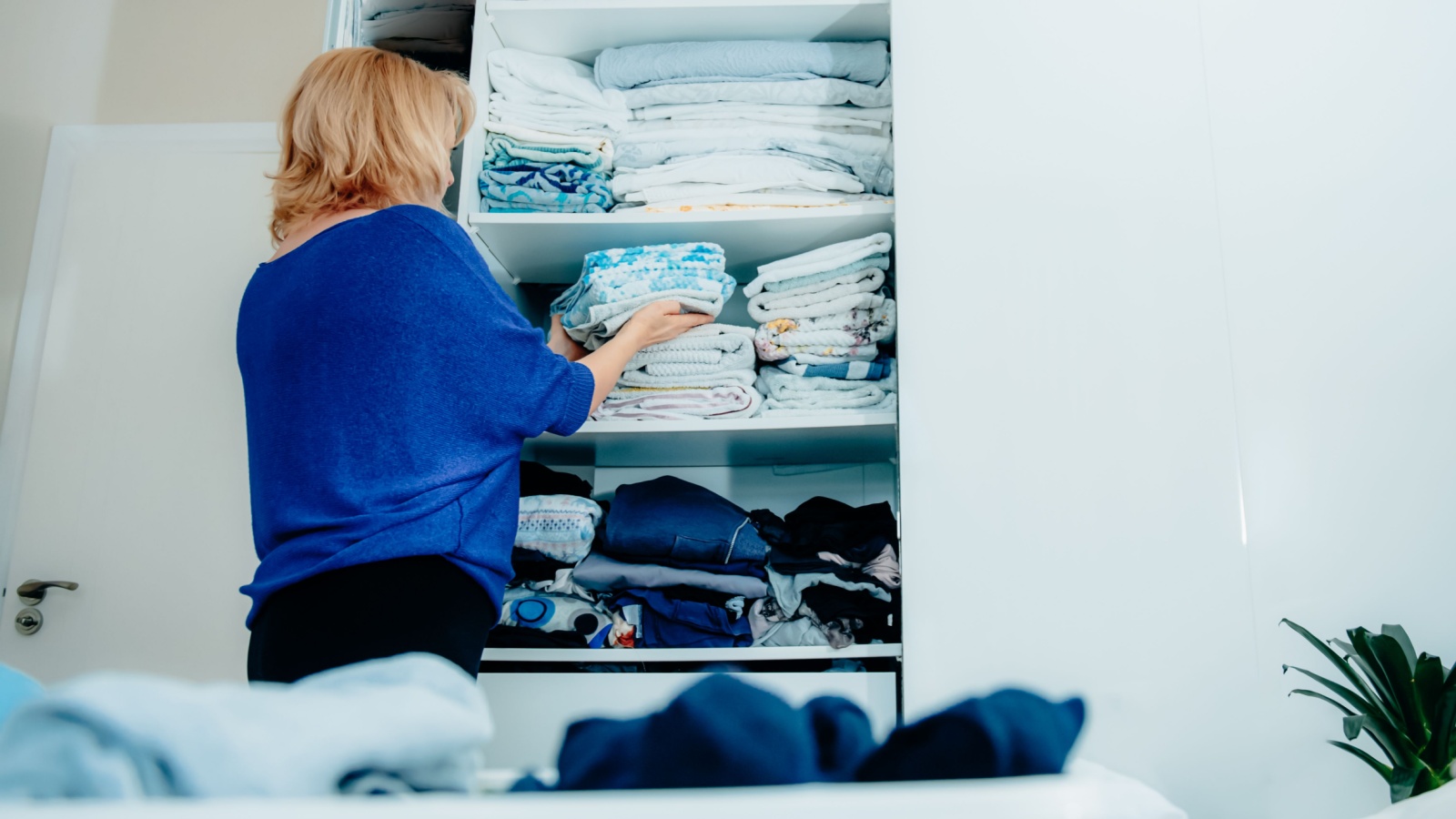 Back view of a woman organizing a wardrobe, holding towels in her hands and putting them on a shelf. Clean up your home space, make your home cozy.