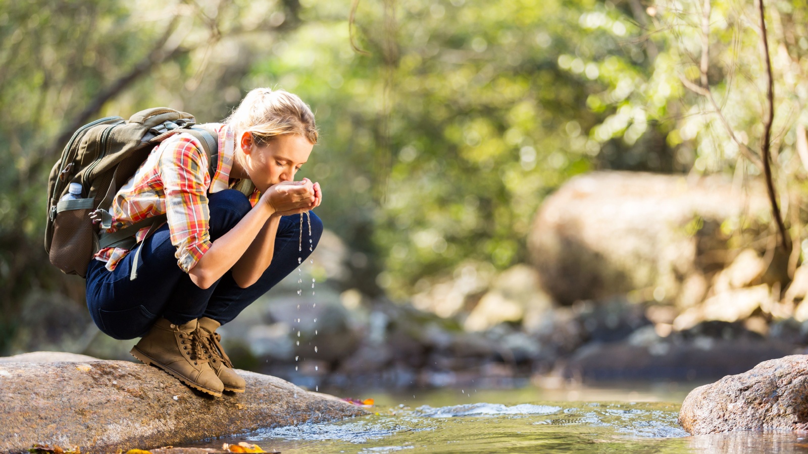 young hiker drinking stream water in mountain