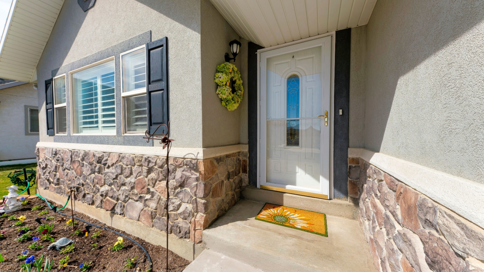 Entrance of a house with wreath beside the glass storm door over the white door with ornate glass