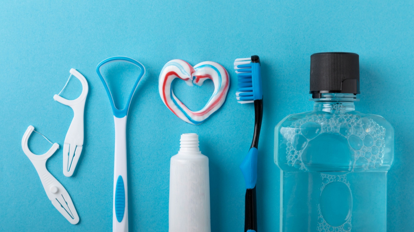 Toothbrush, tongue cleaner, floss, toothpaste tube and mouthwash on blue background with copy space. Flat lay. Dental hygiene. Oral care kit.