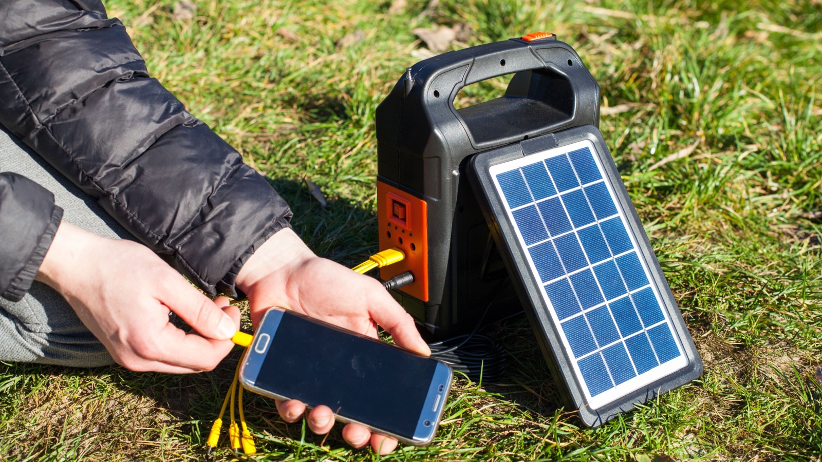 A solar panel charges a phone on a nice sunny day. The phone is in the hands of a man who is charging it. Portable powerbank for hiking and tourism.