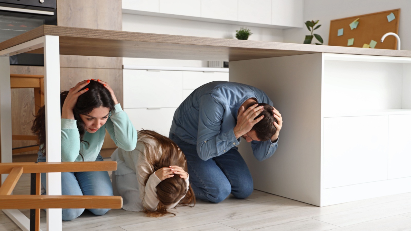 Scared family hiding under dining table during earthquake in kitchen