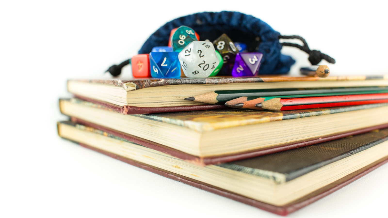 Multicolored dice with dice bag and Pencils on top of three Books