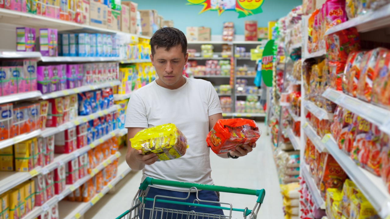 Young caucasian man make choose between two similar goods. Shopping in supermarket or grocery