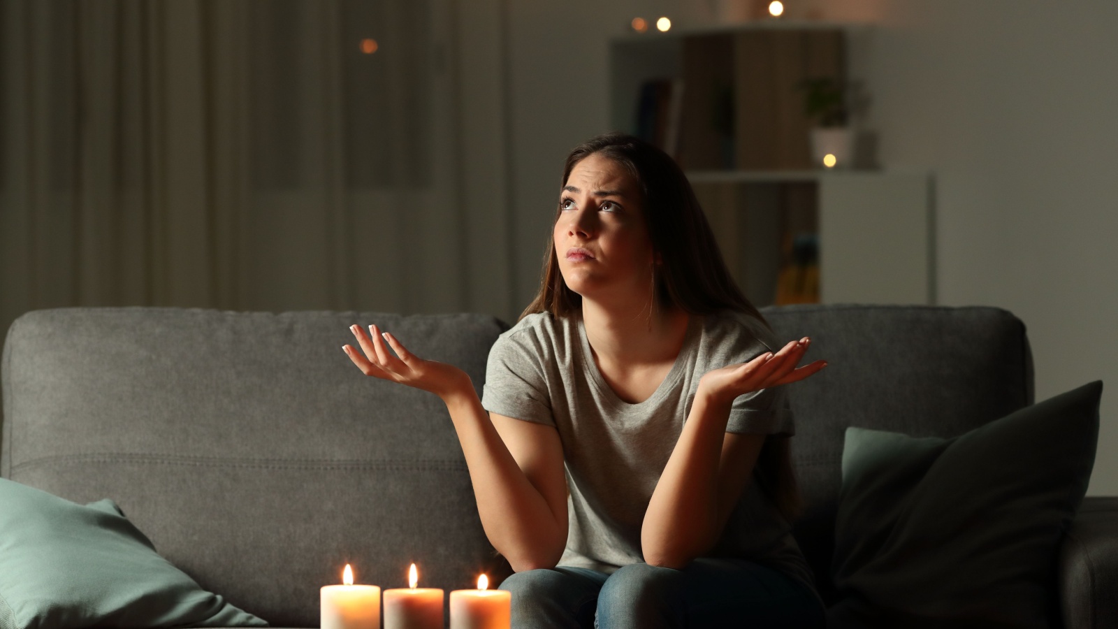 Woman complaining during a blackout sitting on a couch in the living room at home with candles