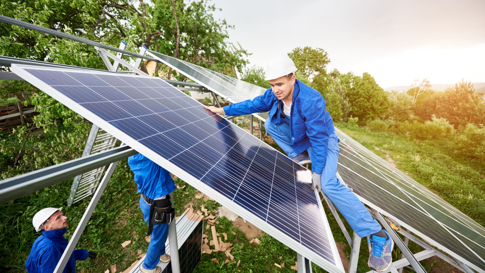 stand-alone solar photo voltaic panel system. Two technicians in hard-hats mounting big shiny solar module on platform 