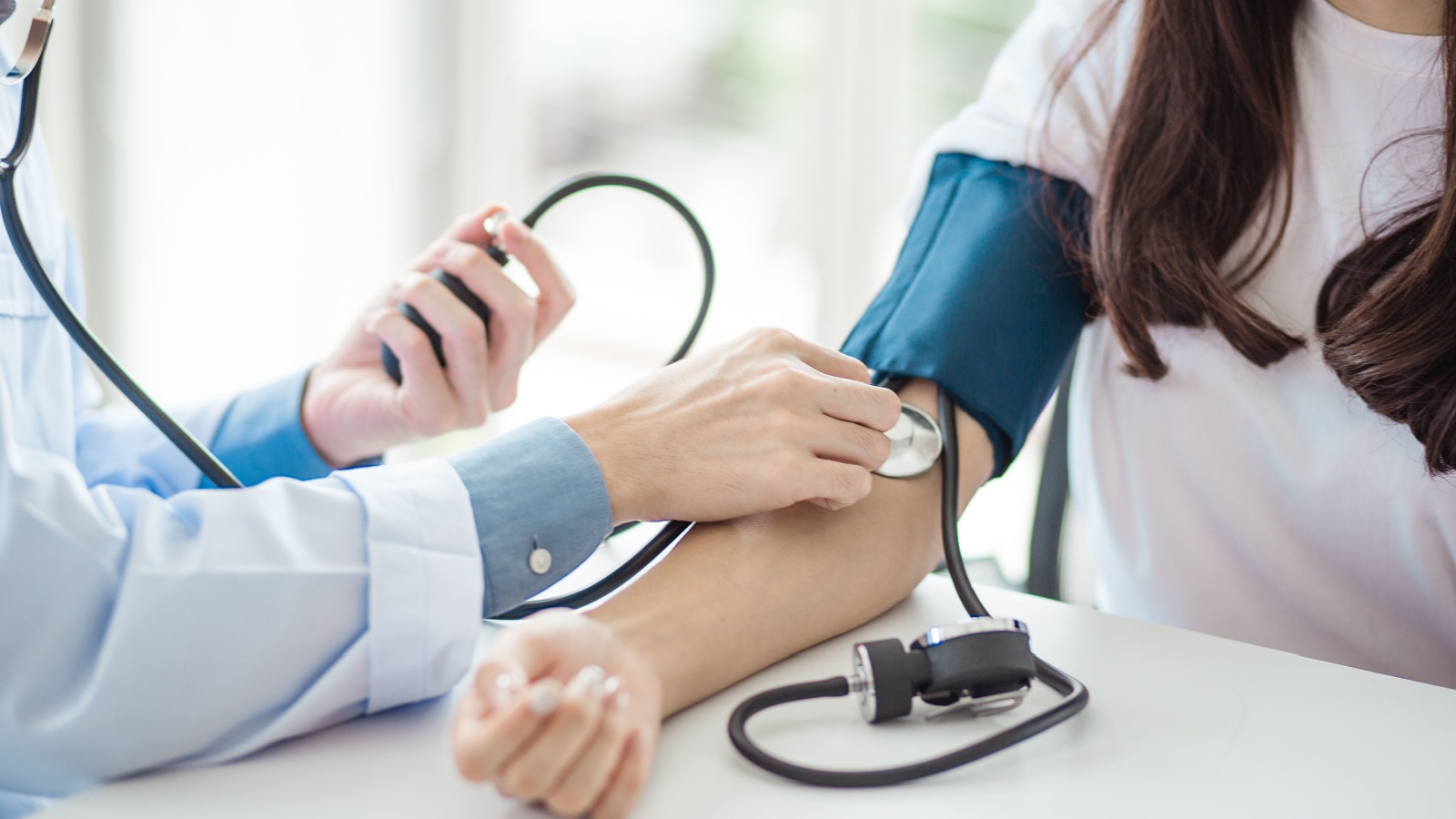 Doctor using sphygmomanometer with stethoscope checking blood pressure to a patient in the hospital.