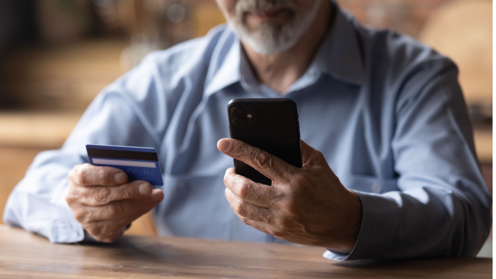 mature man using phone, holding plastic credit or debit card, senior grey haired customer making secure internet payment, shopping or browsing online banking service, entering information