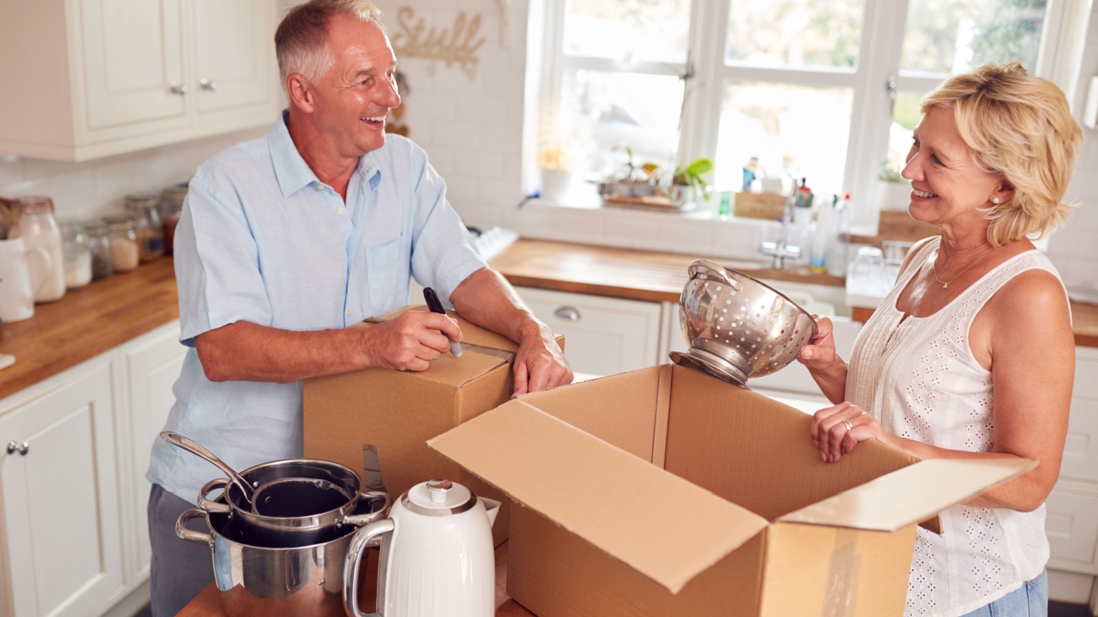 Senior Couple Downsizing In Retirement Packing And Labelling Boxes Ready For Move Into New Home