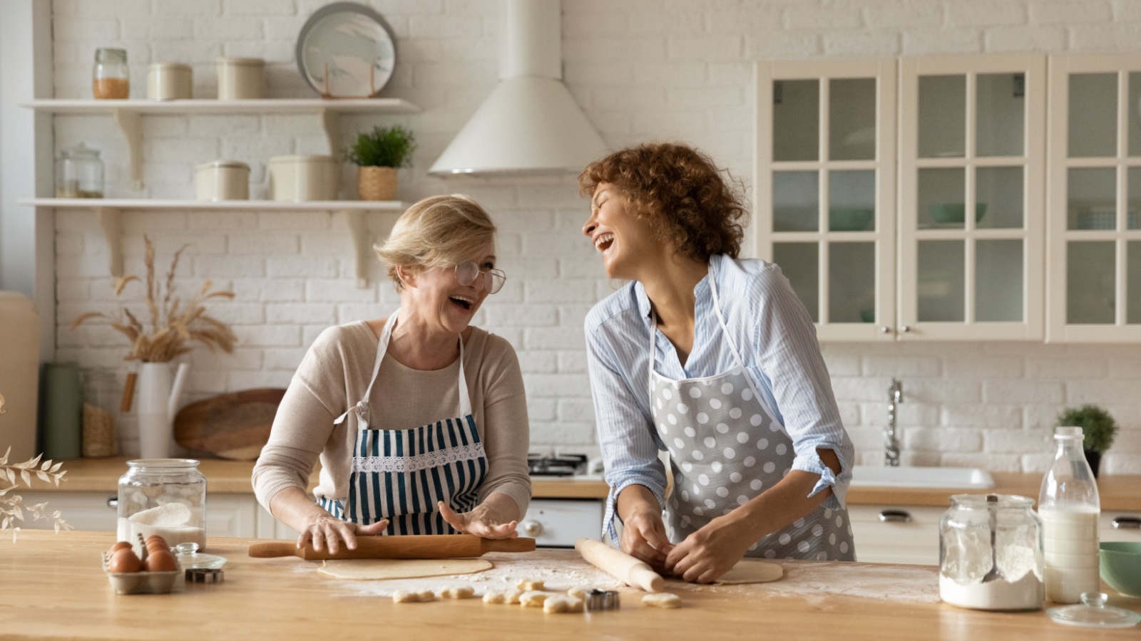 Warm relations. Happy old woman mother pensioner young female daughter grown up kid engaged in baking cookies roll dough at kitchen together laugh have fun. Elderly lady enjoy cooking with adult child, learning new skills