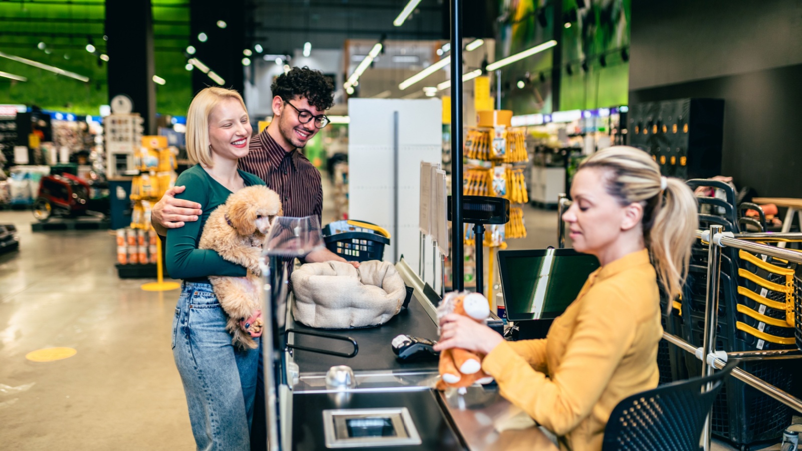 Happy young couple buying accessories and food for their poodle puppy in pet shop.
