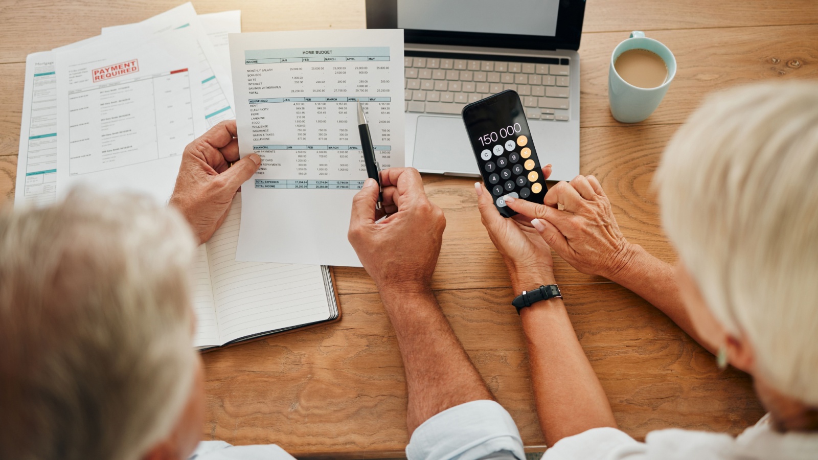 Home budget, finance planning and senior couple calculating their expenses, bills or income during retirement with a calculator, laptop and paper documents from behind.