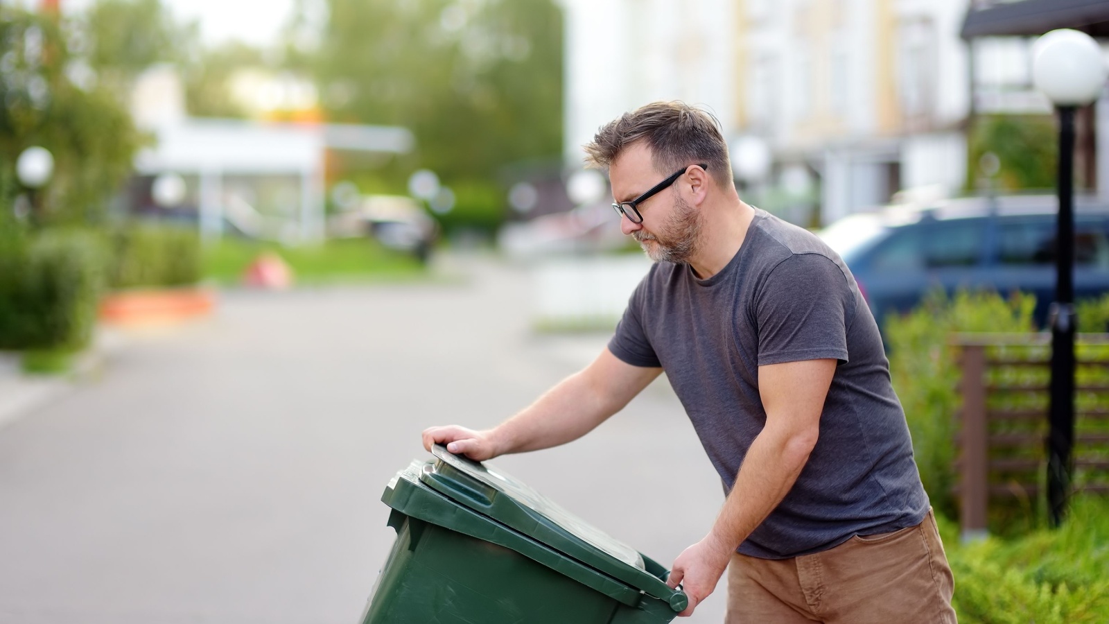 man pulling out a large green plastic garbage container in front of the townhouse to the roadway of the street. Garbage collection and recycling trash, the zero waste concept. Waste managment