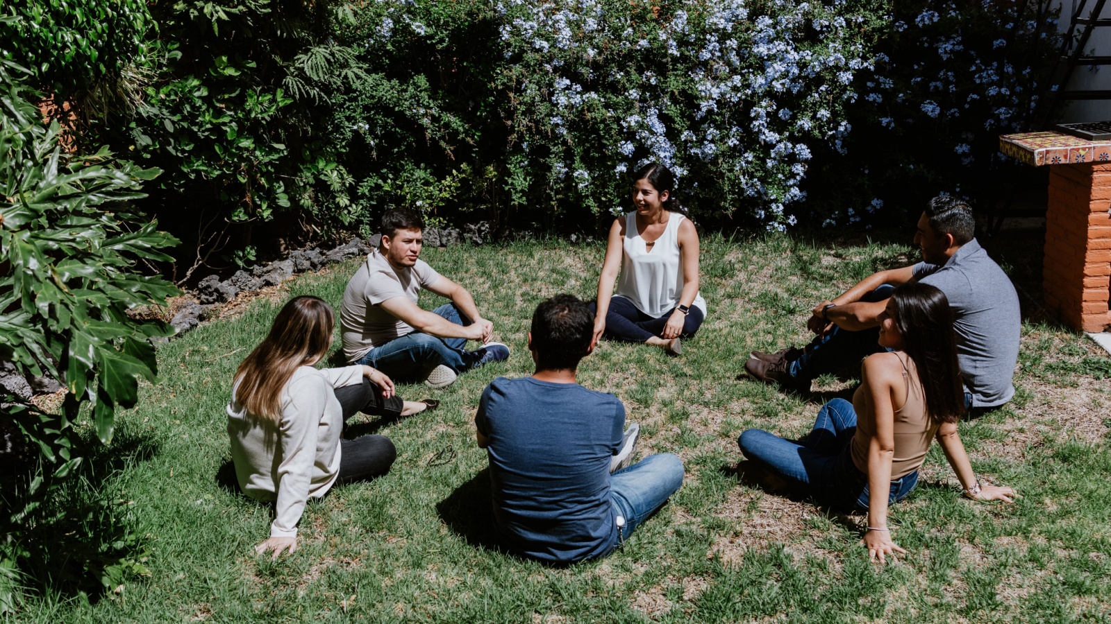 young people seated in circle on grass and participating at group therapy session, community