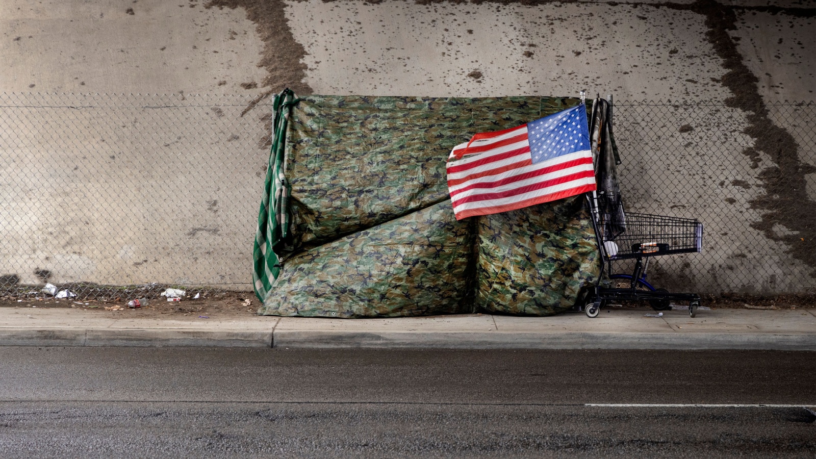 An American flag at a homeless tent made of camouflage tarp at a road underpass