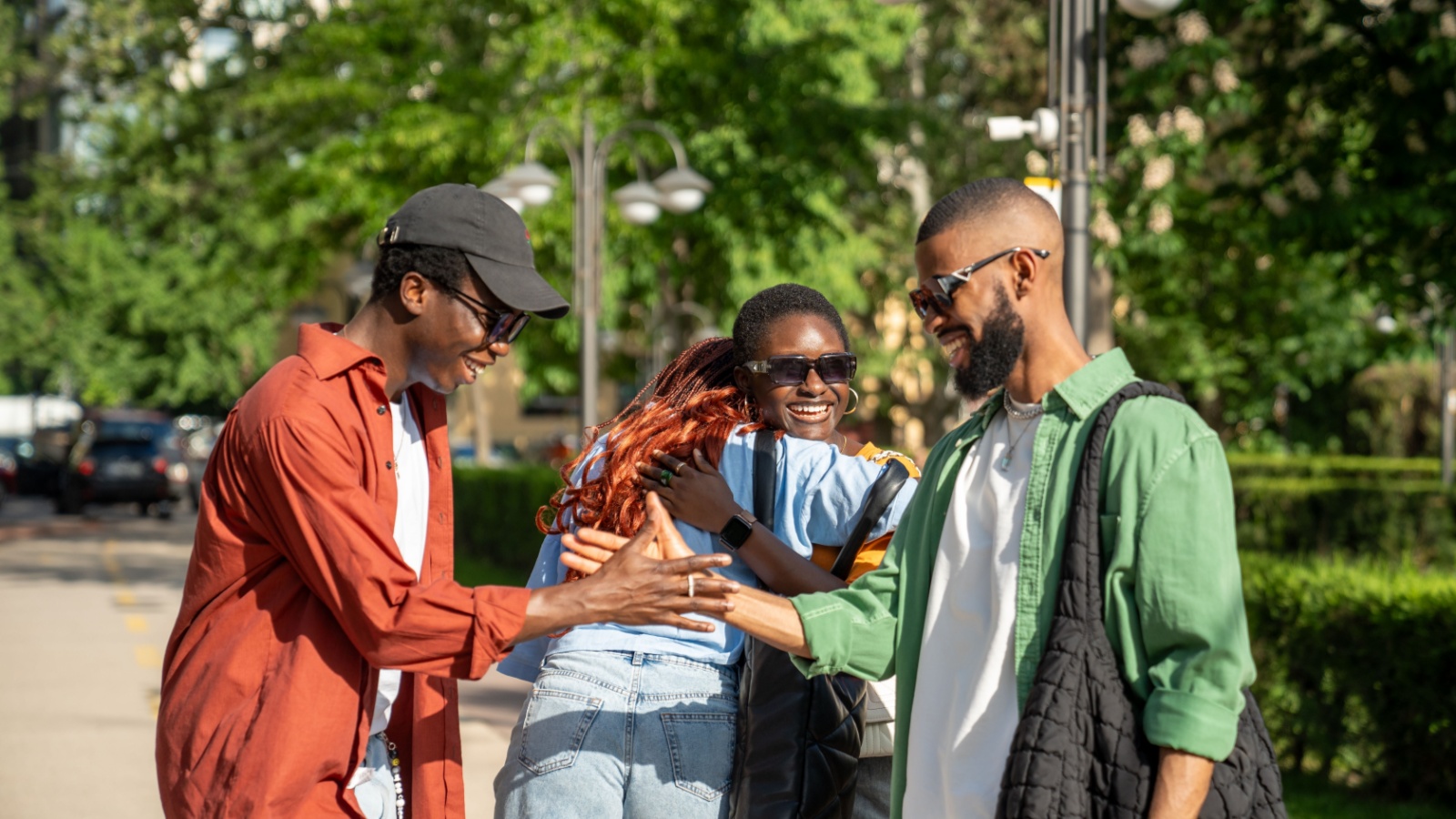 Joyous hello of african american friends on street. Happy group of black students with good mood embrace each other as meet to spend time together.Two guys shake hands, girls smile hug, see each other