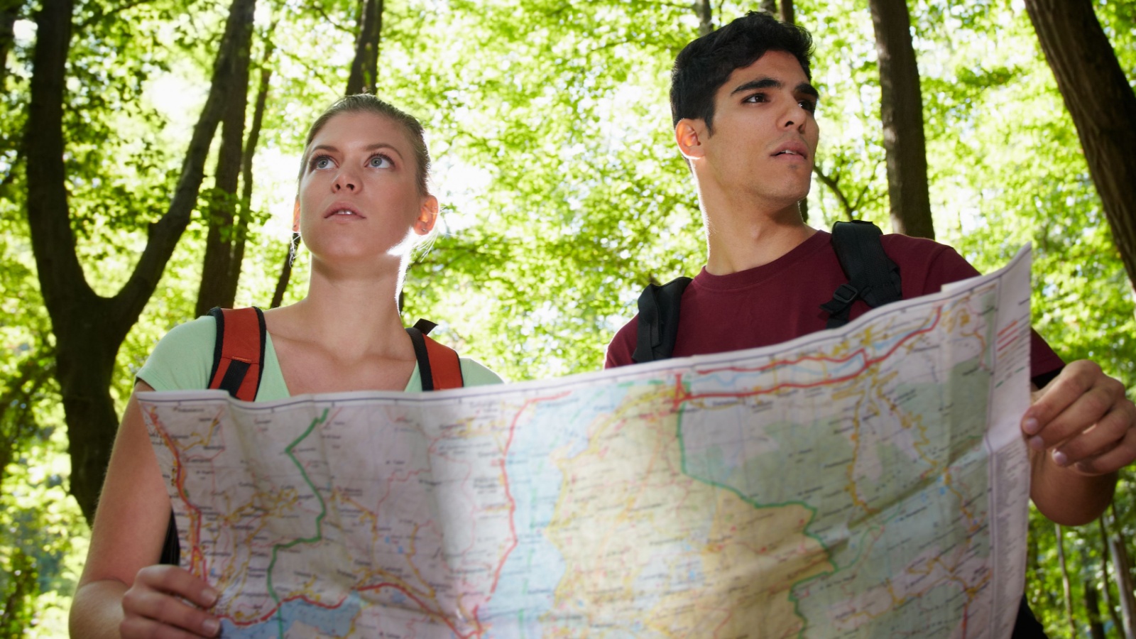 young man and woman looking for safe zones during an attack, got lost during hiking excursion and look for destination on map.