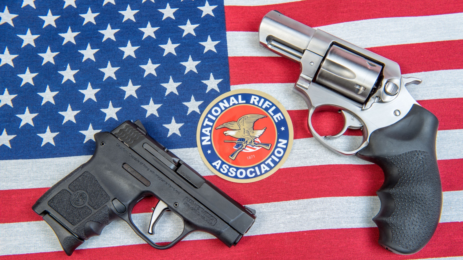 A NRA sticker with a semi automatck and revolver handguns on an American flag.