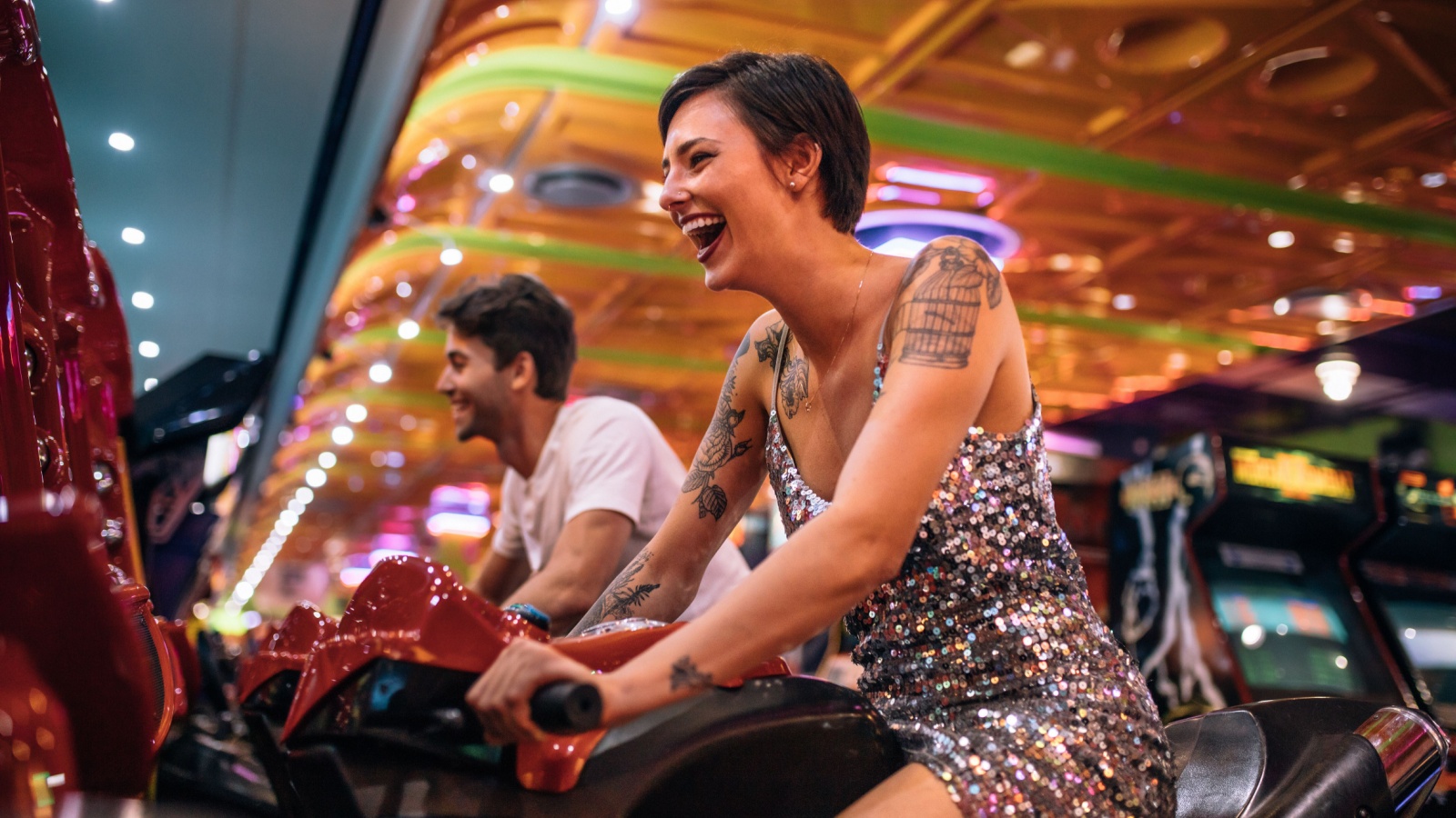 Excited woman playing a racing game sitting on an arcade racing bike. Couple enjoying arcade racing games at a gaming parlour.