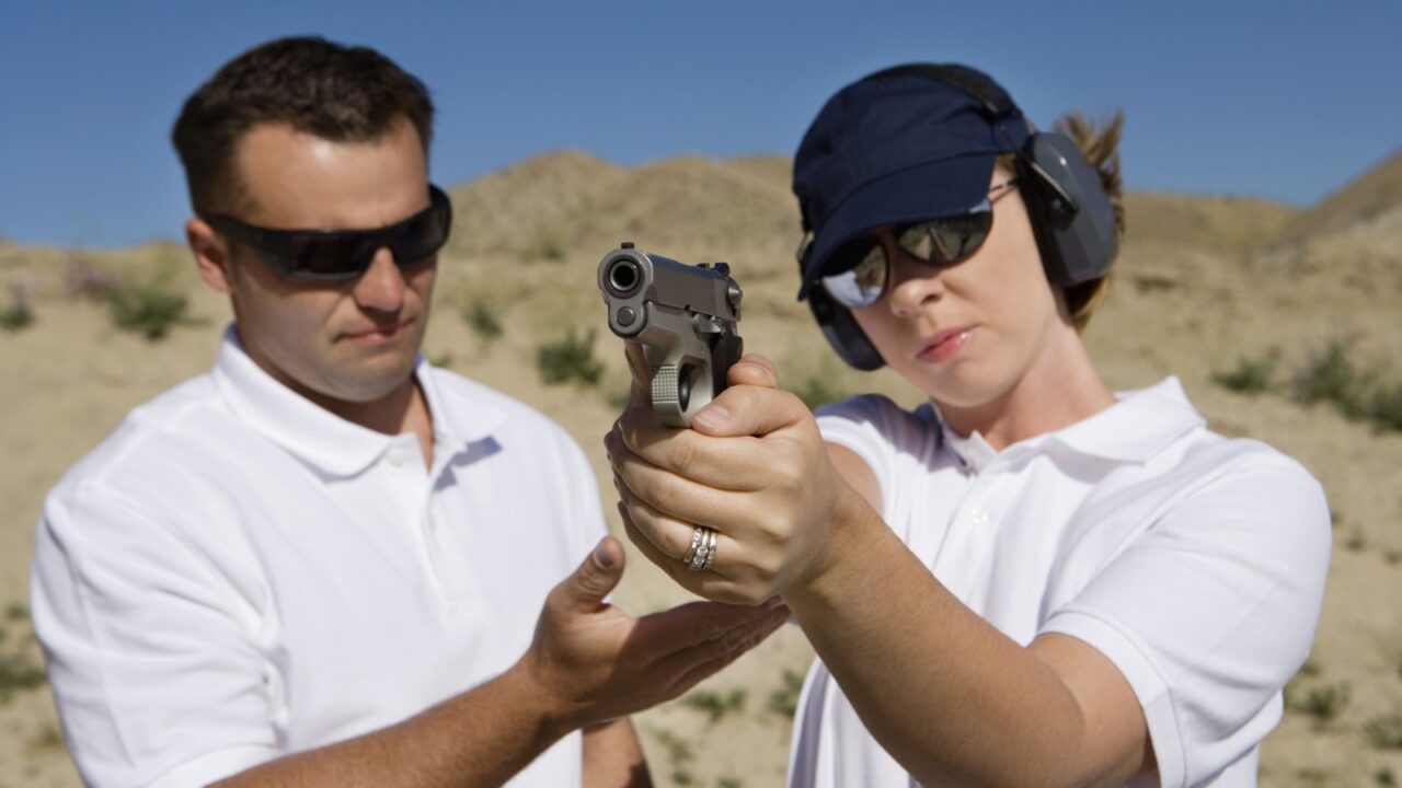 Trainer helping young woman to aim with handgun at combat training