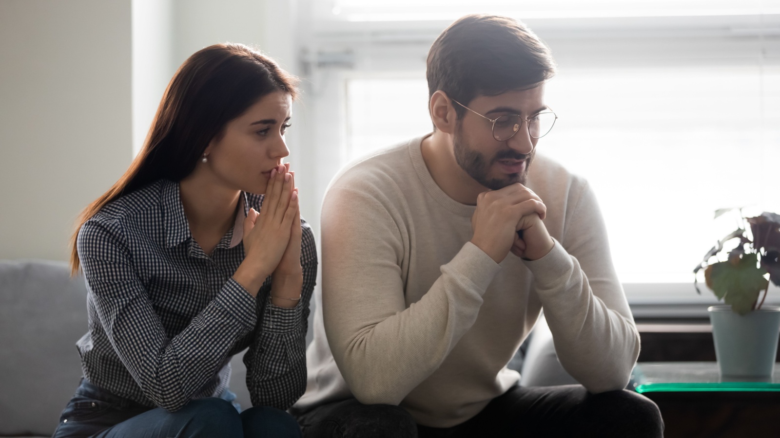 Worrying woman sitting on sofa near offended husband on psychological therapy session, saying sorry. Guilty young wife apologizing for misunderstanding to abused upset man. Family problems