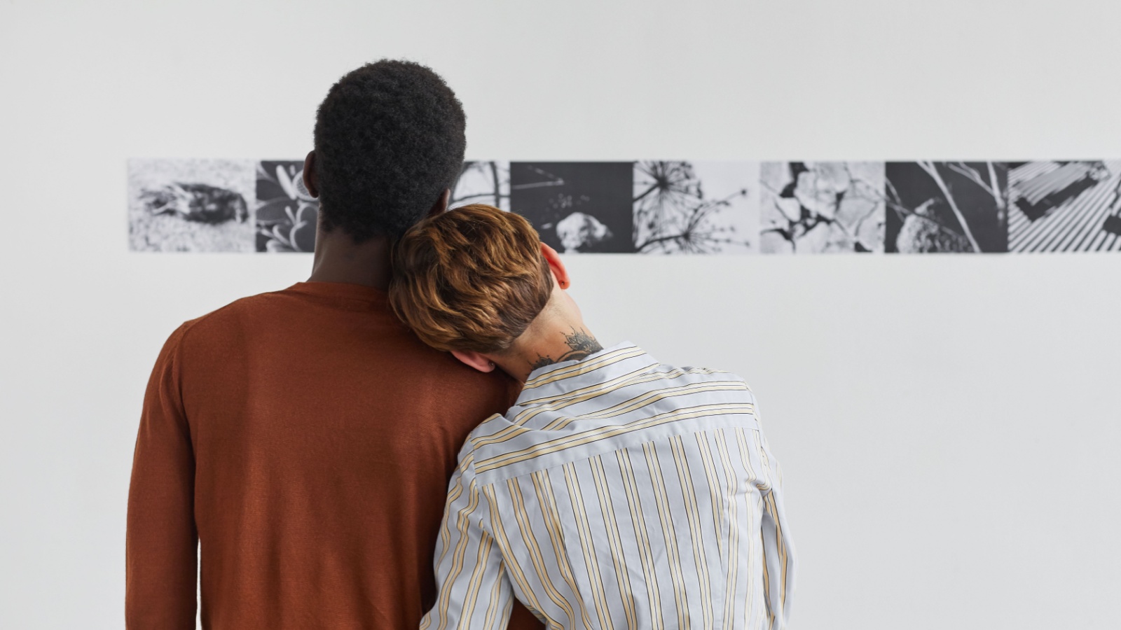 mixed-race couple embracing while looking at paintings at modern art gallery exhibition