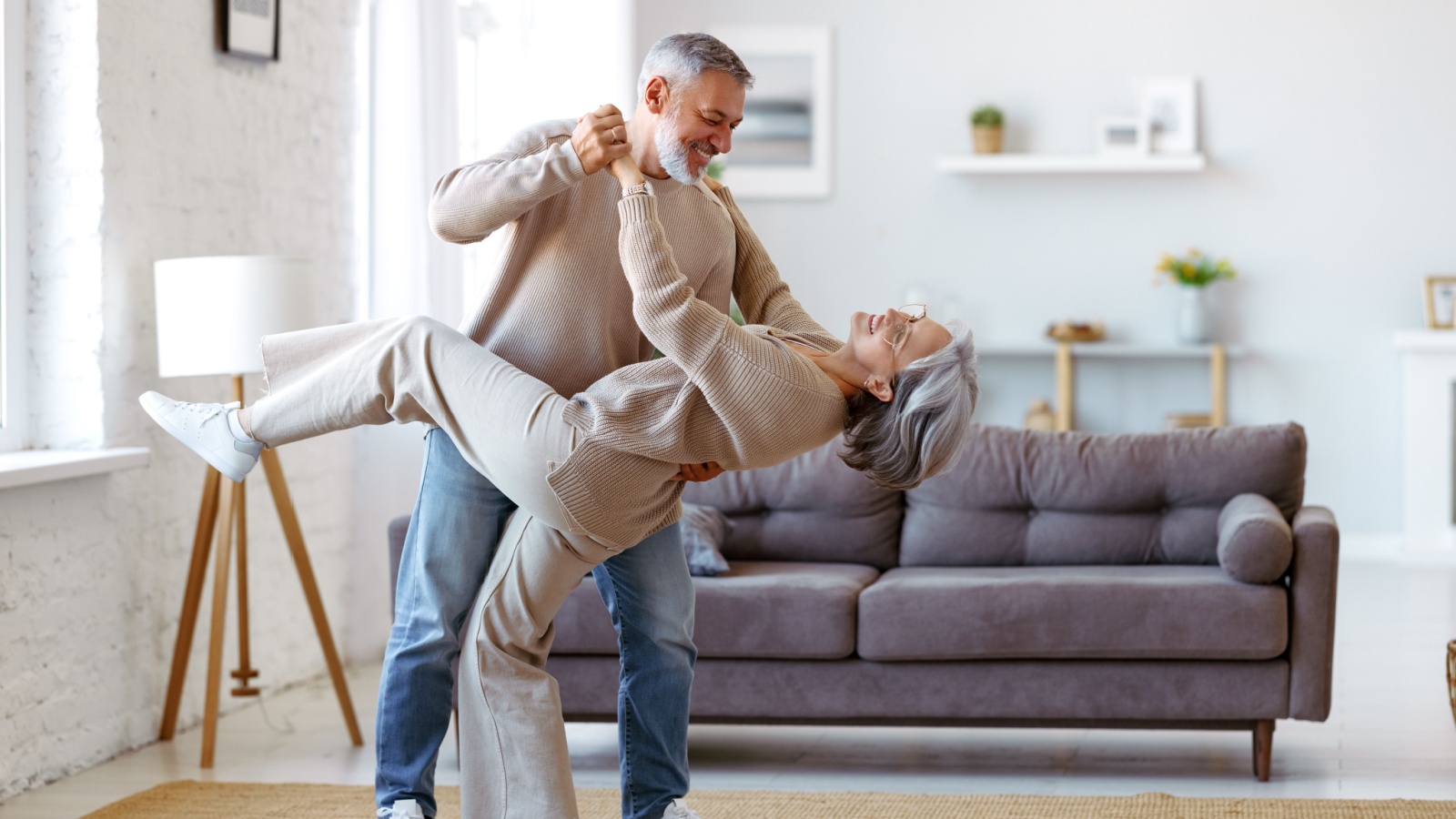 Keep moving. Romantic senior family couple wife and husband dancing to music together in living room, smiling laughing retired man and woman having fun, enjoying free time together at home