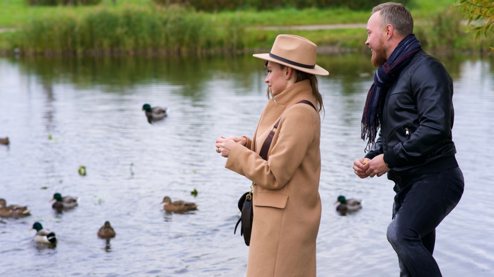 Happy romantic couple in love, beautiful young woman and handsome man is dating, walking together outdoors in park and feeding birds, ducks in a lake or pond. Happiness