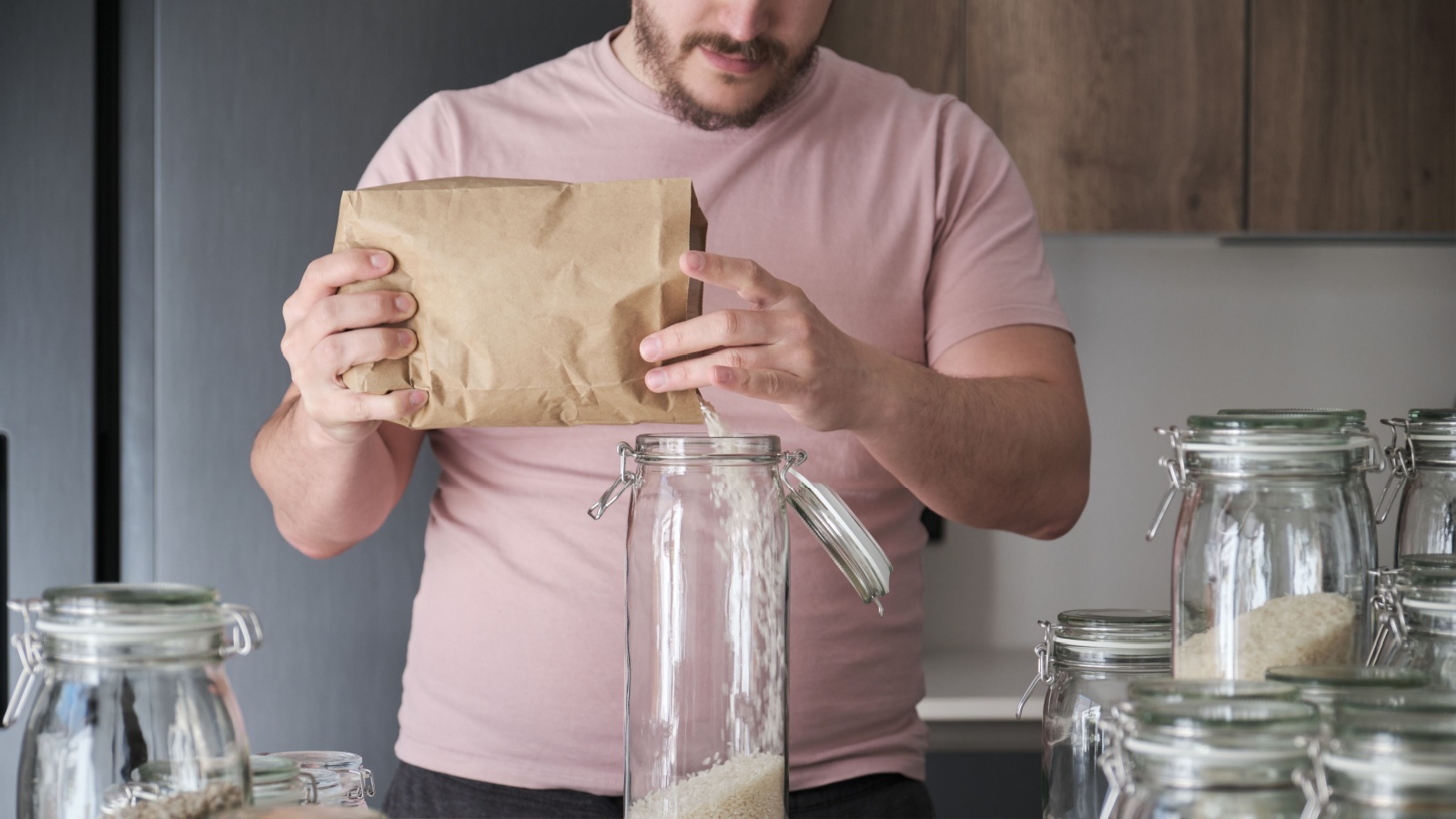 man filling up a jar with round grain rice from a paper bag. Food in bulk delivery.