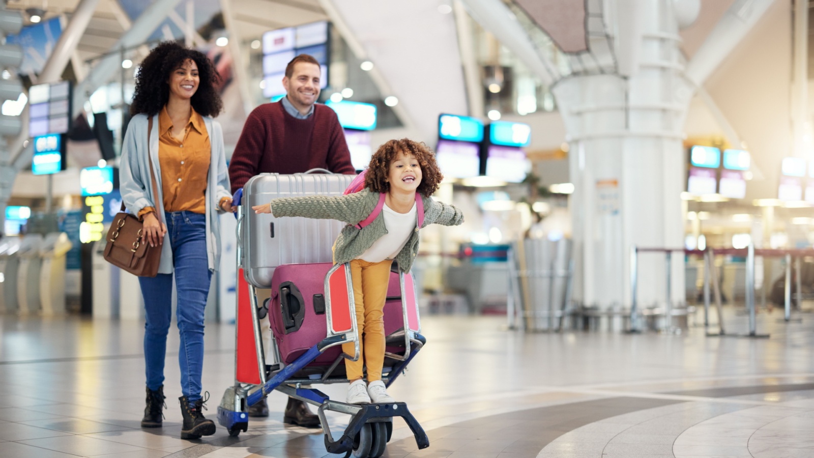 Airport, family and child excited for flight with suitcase trolley on holiday, vacation or immigration journey and travel. Luggage of mother, father or diversity parents with girl kid flying in lobby