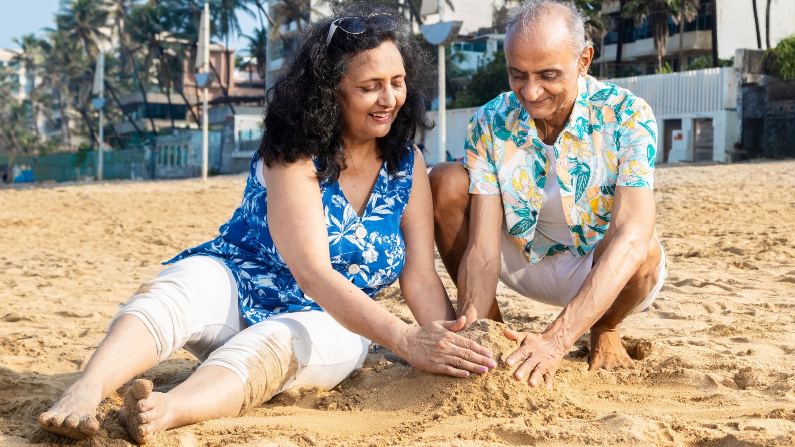 Happy indian senior couple making sand castle or home at the beach enjoying vacation.