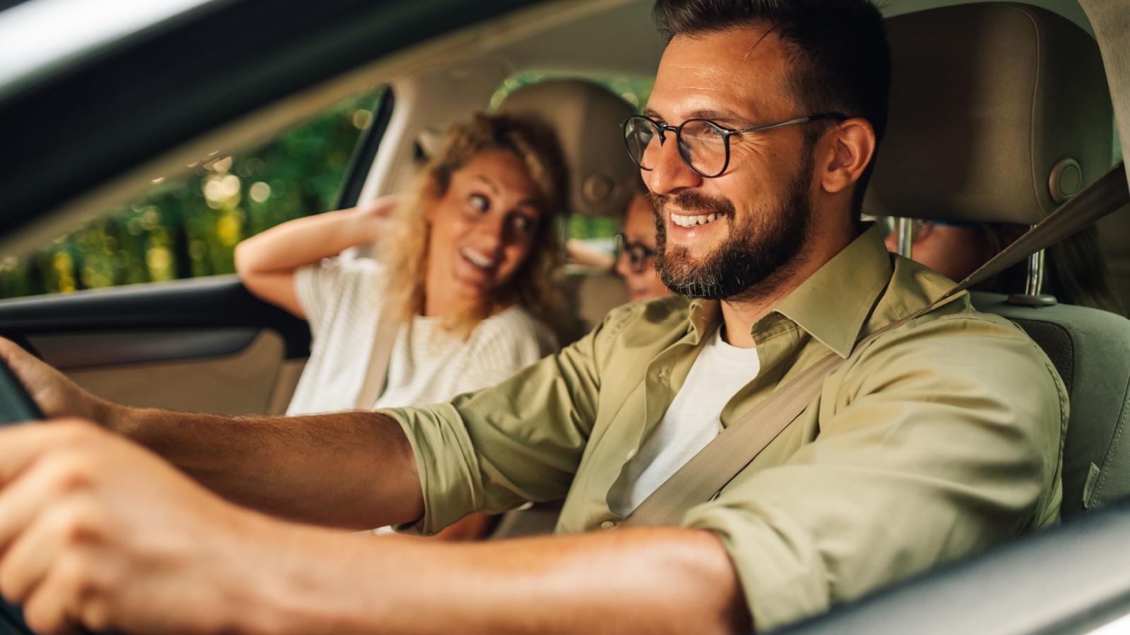 father driving a car while the whole family of four is going on a weekend trip away from the city. Parents making a road trip with their daughters in their new car. Transport and safety.