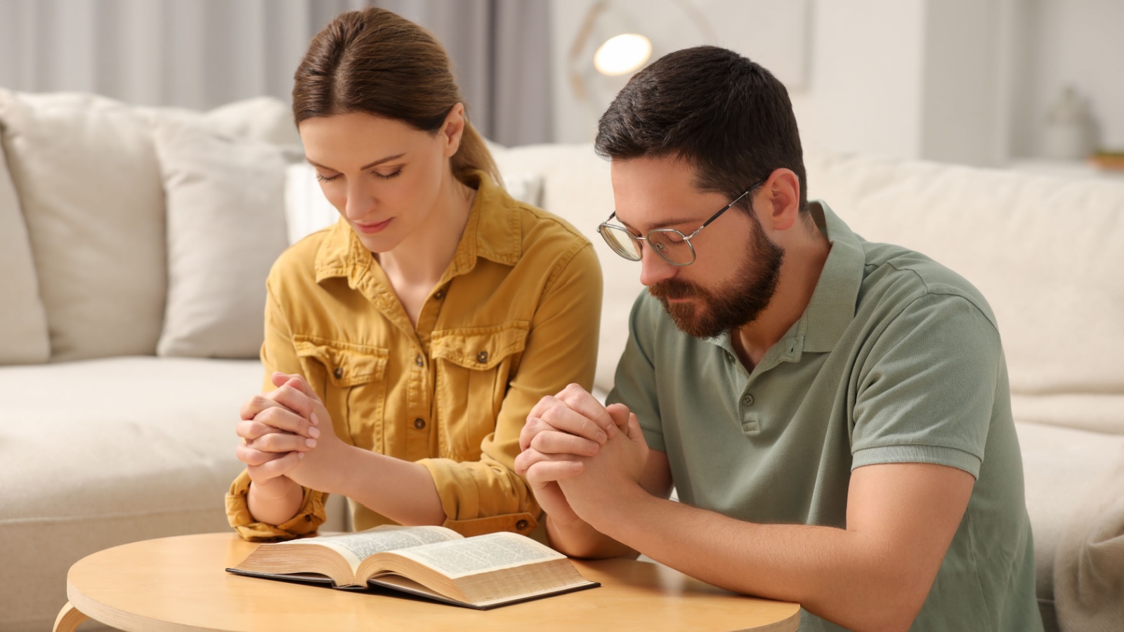 Family couple praying over Bible together at table indoors