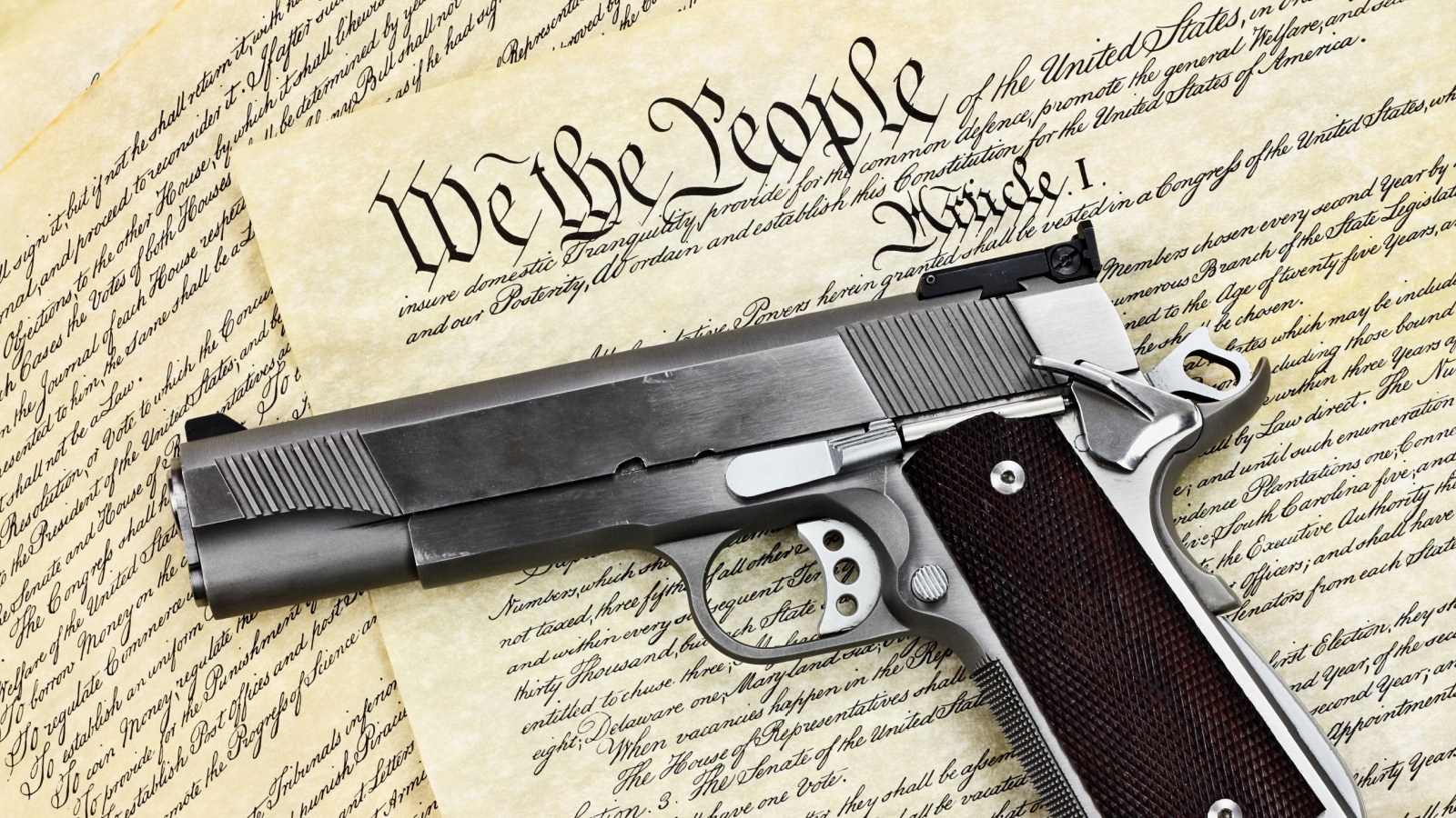 Handgun lying over a copy of the United States constitution with the words "We the People" visible. 2nd amendment